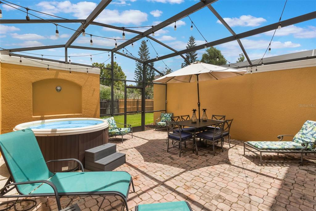 A patio features a hot tub, outdoor dining set with an umbrella, and lounge chairs — 4733 VERO BEACH PLACE, KISSIMMEE, FL
