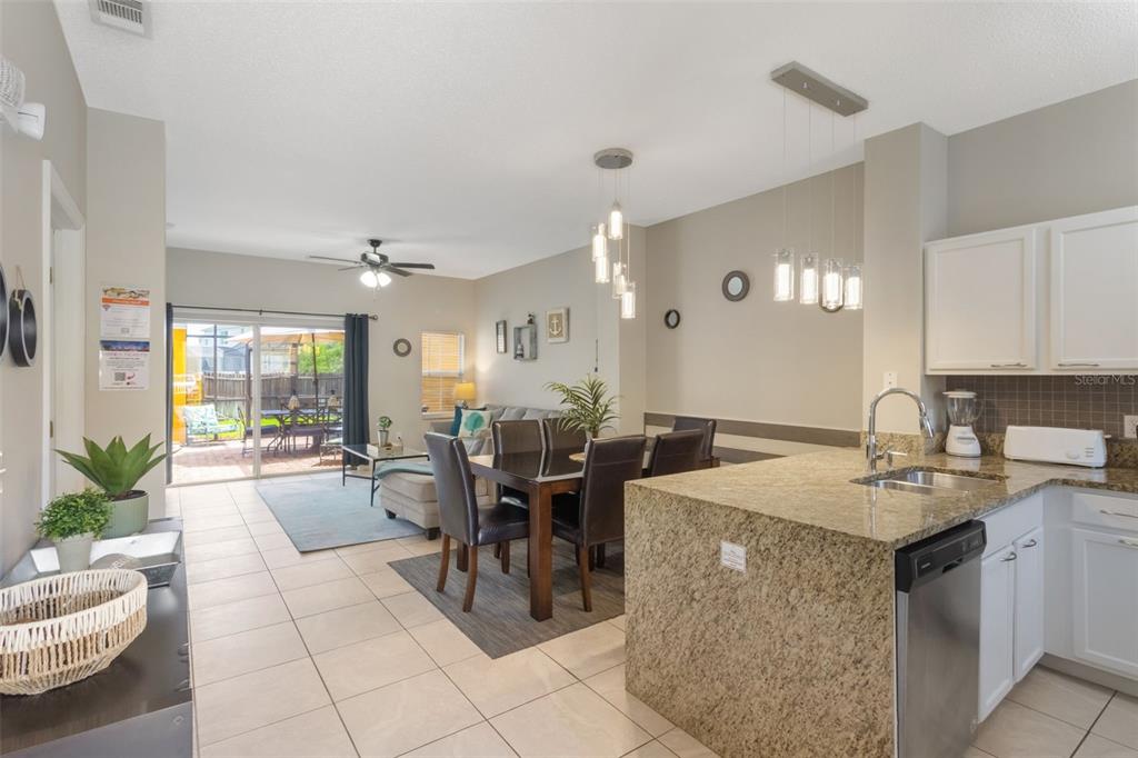 An open-concept kitchen with granite countertops overlooks a dining area and living room with patio access — 4733 VERO BEACH PLACE, KISSIMMEE, FL