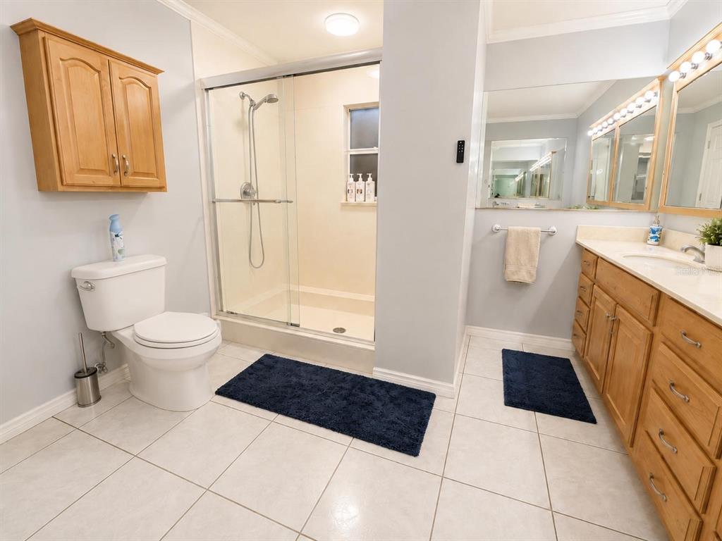 A bathroom features a walk-in shower, a toilet, a wooden vanity, and light-colored tile flooring — 1205 LISA LANE, OKEECHOBEE, FL