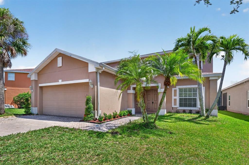 A two-story tan house with a two-car garage, palm trees, and a paved driveway — 8083 SILVER BIRCH WAY, LEHIGH ACRES, FL