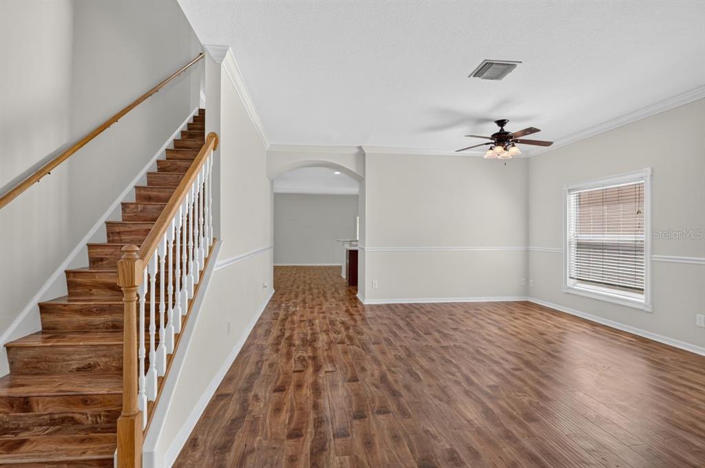 An empty living room features wood-look flooring, a staircase with white railings, and a ceiling fan — 8083 SILVER BIRCH WAY, LEHIGH ACRES, FL