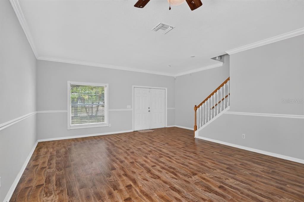 A living room with light gray walls, wood-look flooring, a white staircase, and double doors — 8083 SILVER BIRCH WAY, LEHIGH ACRES, FL