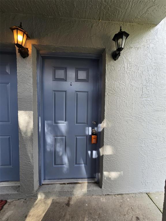 A blue six-panel front door with a lockbox is flanked by two outdoor wall lamps — 7186 E BANK DRIVE UNIT 7186, TAMPA, FL