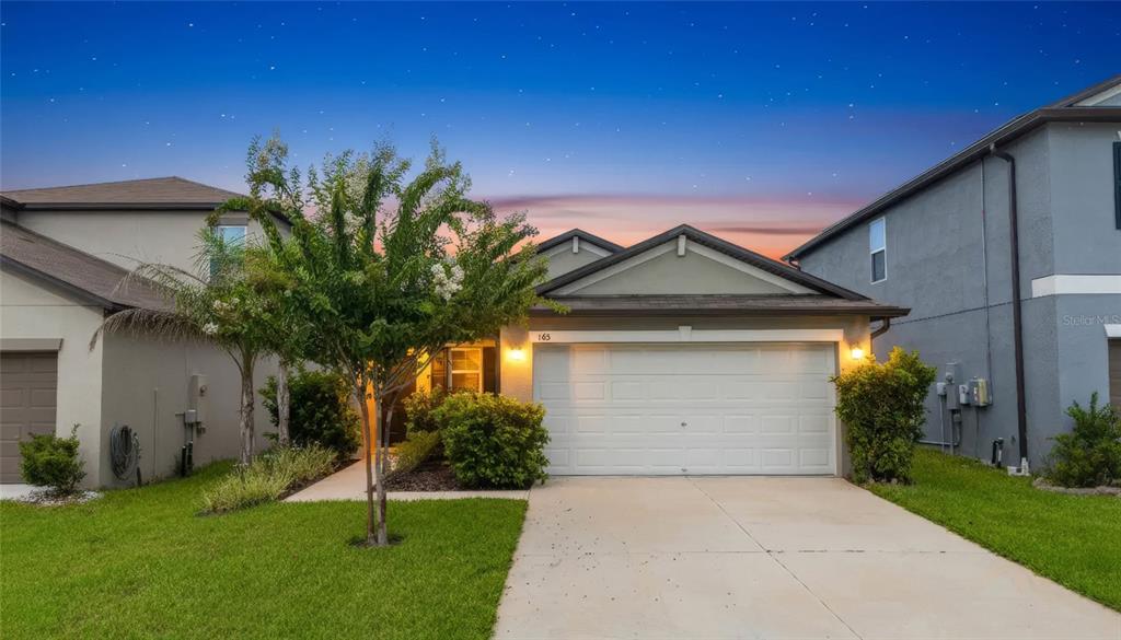 A single-story suburban house with a two-car garage and a landscaped front yard at dusk — 165 ARGYLL DRIVE, SPRING HILL, FL