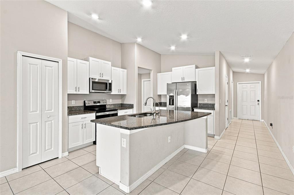 A kitchen with white cabinets, granite countertops, a center island, and light-colored tile flooring — 165 ARGYLL DRIVE, SPRING HILL, FL