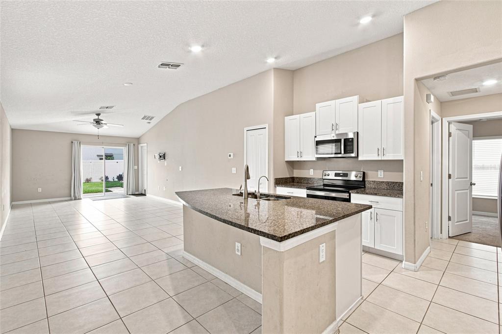 A kitchen with white cabinets and granite countertops overlooks an open-concept living area with tile — 165 ARGYLL DRIVE, SPRING HILL, FL