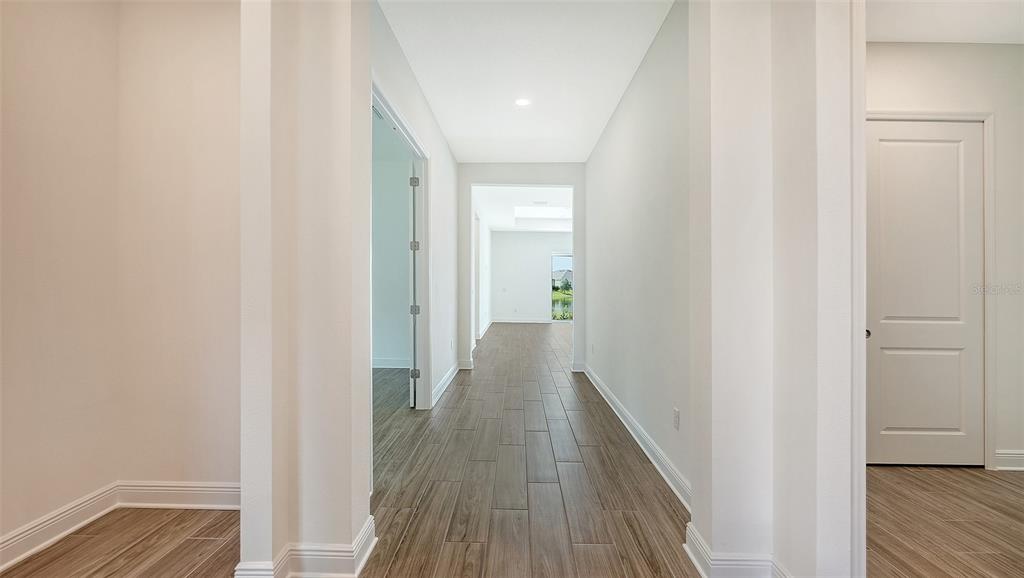A hallway with wood-look tile flooring leads to a doorway with a view of greenery — 4420 WATER LANDING WAY, PARRISH, FL