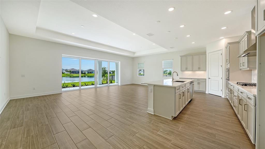 An open-concept kitchen and living area with light wood-look tile floors and sliding glass doors — 4420 WATER LANDING WAY, PARRISH, FL