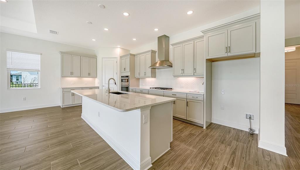 A modern kitchen features light gray cabinetry, a large center island, and wood-look tile flooring — 4420 WATER LANDING WAY, PARRISH, FL