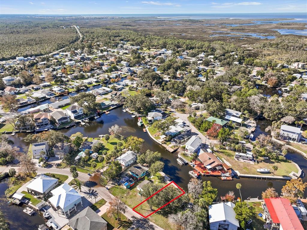 An aerial view shows a vacant, tree-covered lot outlined in red along a residential canal — 7259 TROPICAL DRIVE, WEEKI WACHEE, FL