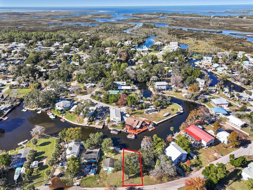 An aerial view shows a vacant, tree-covered lot outlined in red near a coastal waterway — 7259 TROPICAL DRIVE, WEEKI WACHEE, FL