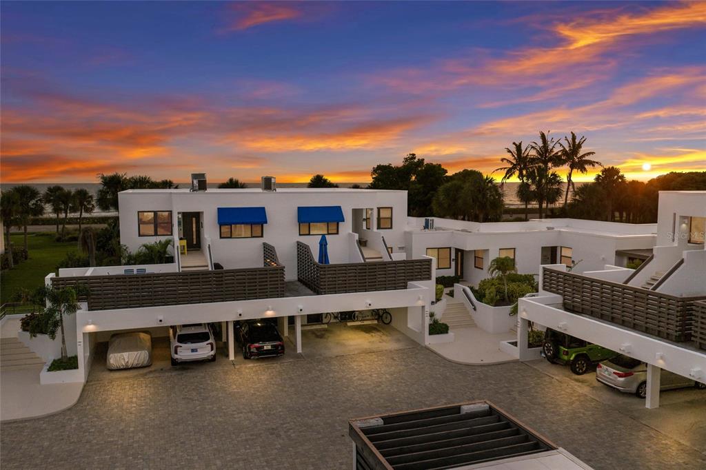 An exterior view of a modern white multi-unit building with covered parking and sunset sky — 713 BAYPORT WAY UNIT 713, LONGBOAT KEY, FL