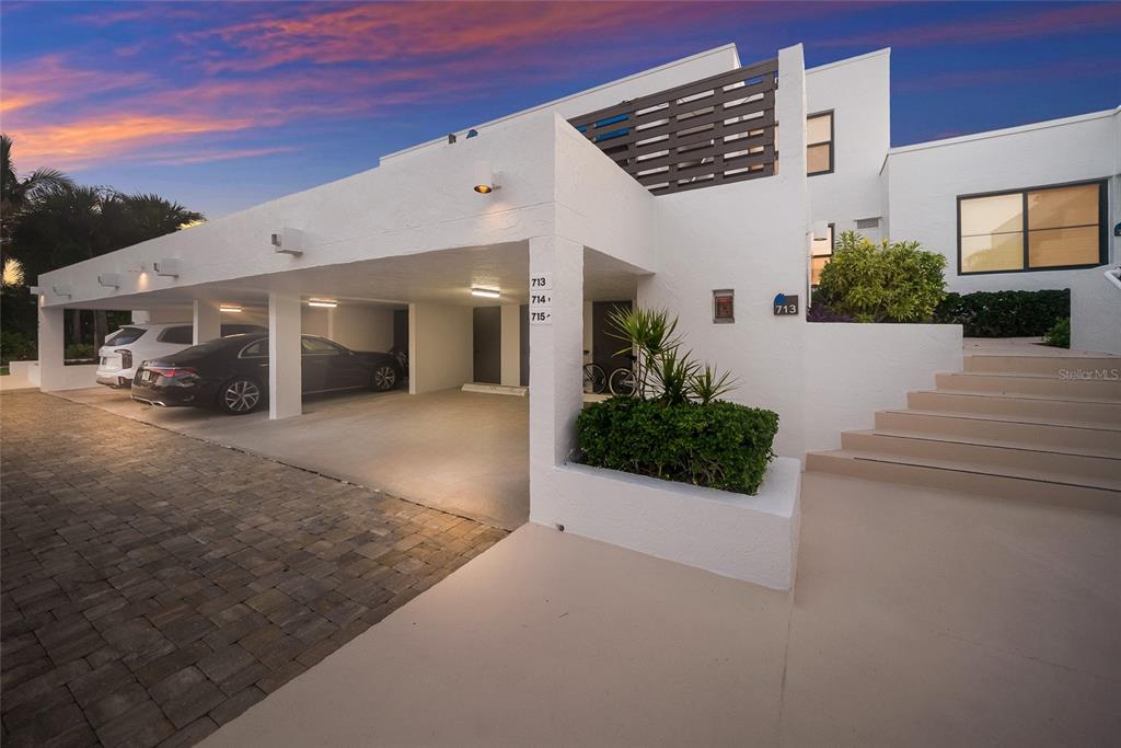 A modern white building features a covered parking area, stairs, and a landscaped planter — 713 BAYPORT WAY UNIT 713, LONGBOAT KEY, FL