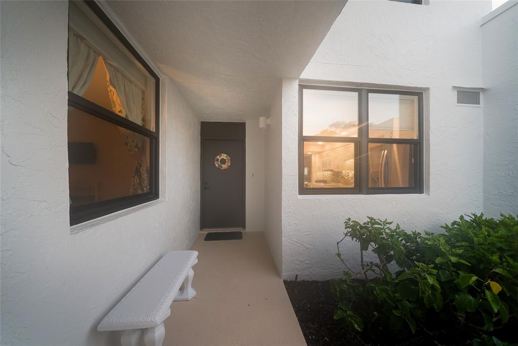 A white exterior entryway features a dark front door, a stone bench, and two windows — 713 BAYPORT WAY UNIT 713, LONGBOAT KEY, FL