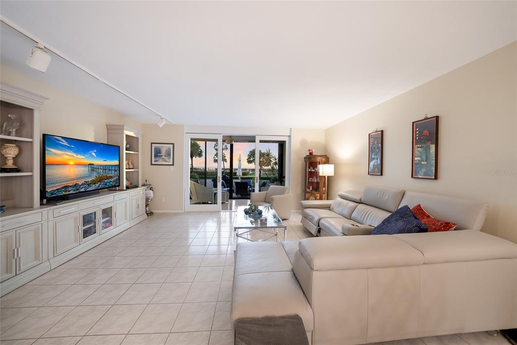 A living room with light tile floors, a large sectional sofa, and a wall-mounted television — 713 BAYPORT WAY UNIT 713, LONGBOAT KEY, FL