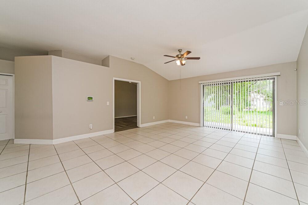 An empty living room features light-colored tile flooring, vaulted ceilings, and sliding glass patio doors — 10119 PINK CARNATION COURT, ORLANDO, FL