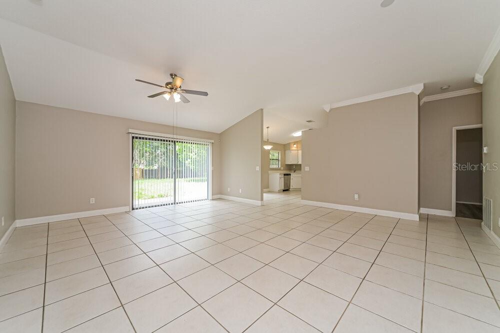 A spacious living room features light-colored tile flooring, a vaulted ceiling, and sliding glass doors — 10119 PINK CARNATION COURT, ORLANDO, FL