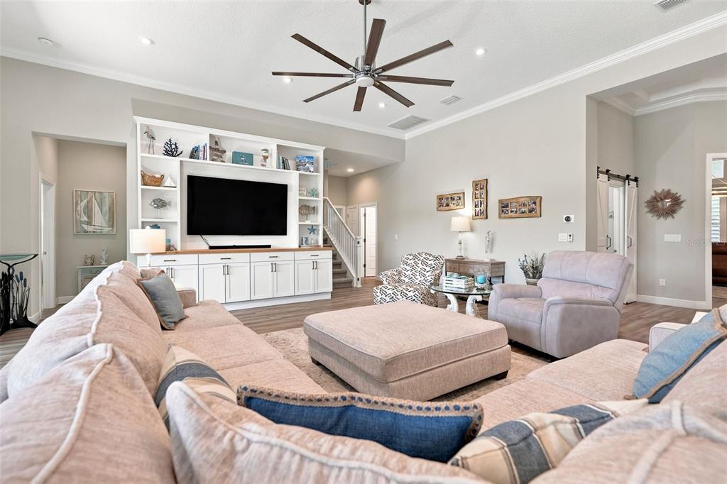 A spacious living room features a large sectional sofa, an ottoman, and sliding glass doors — 4093 EPIC COVE, LAND O LAKES, FL