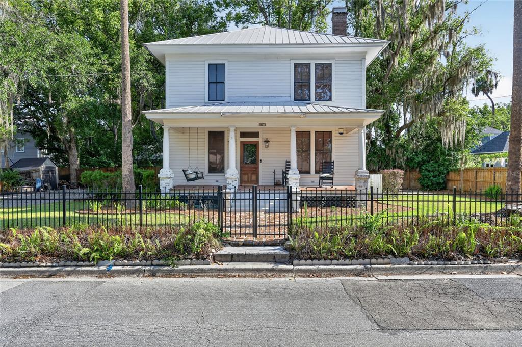 A two-story white house with a metal roof and a front porch behind a fence — 819 SE 2ND STREET, OCALA, FL