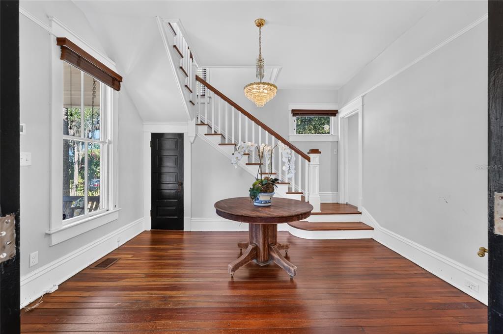 A foyer features hardwood floors, a central wooden table, and a staircase with white railings — 819 SE 2ND STREET, OCALA, FL