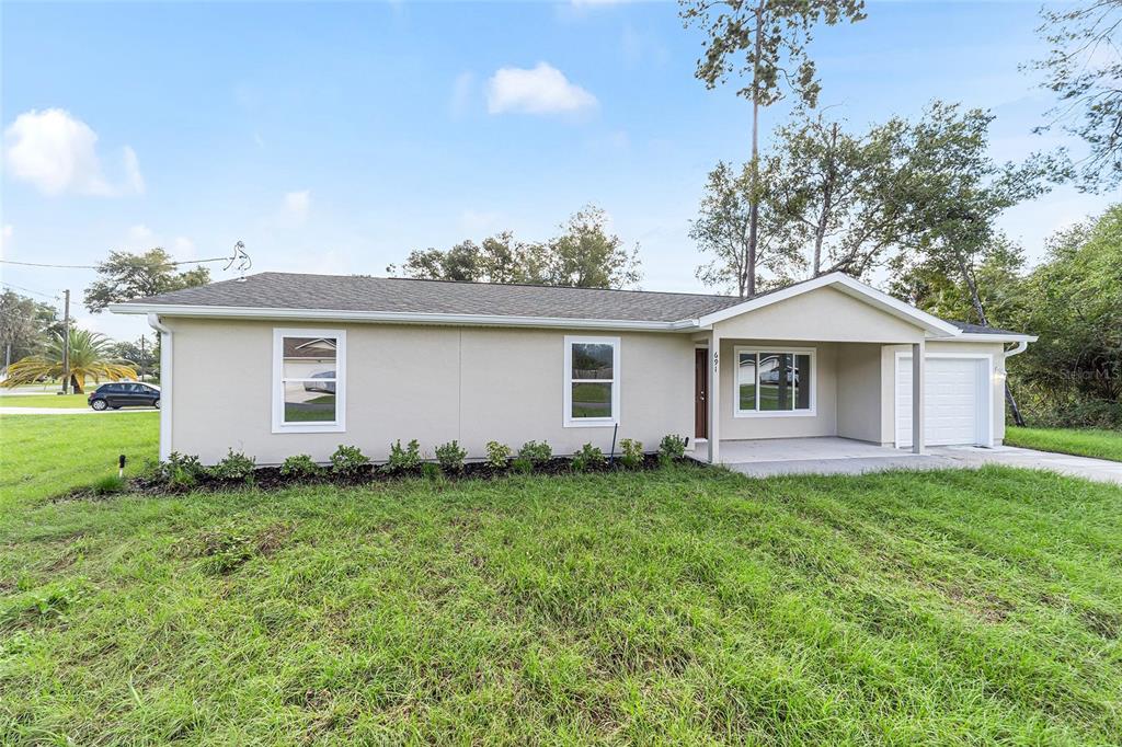 A single-story house with a light-colored exterior, a front-facing garage, and a large grassy yard — 23827 SW BEAVER DRIVE, DUNNELLON, FL