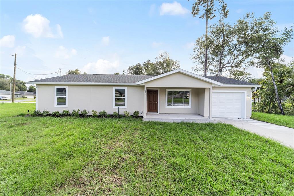 A single-story house with a white garage and concrete driveway sits on a grassy lot — 23827 SW BEAVER DRIVE, DUNNELLON, FL