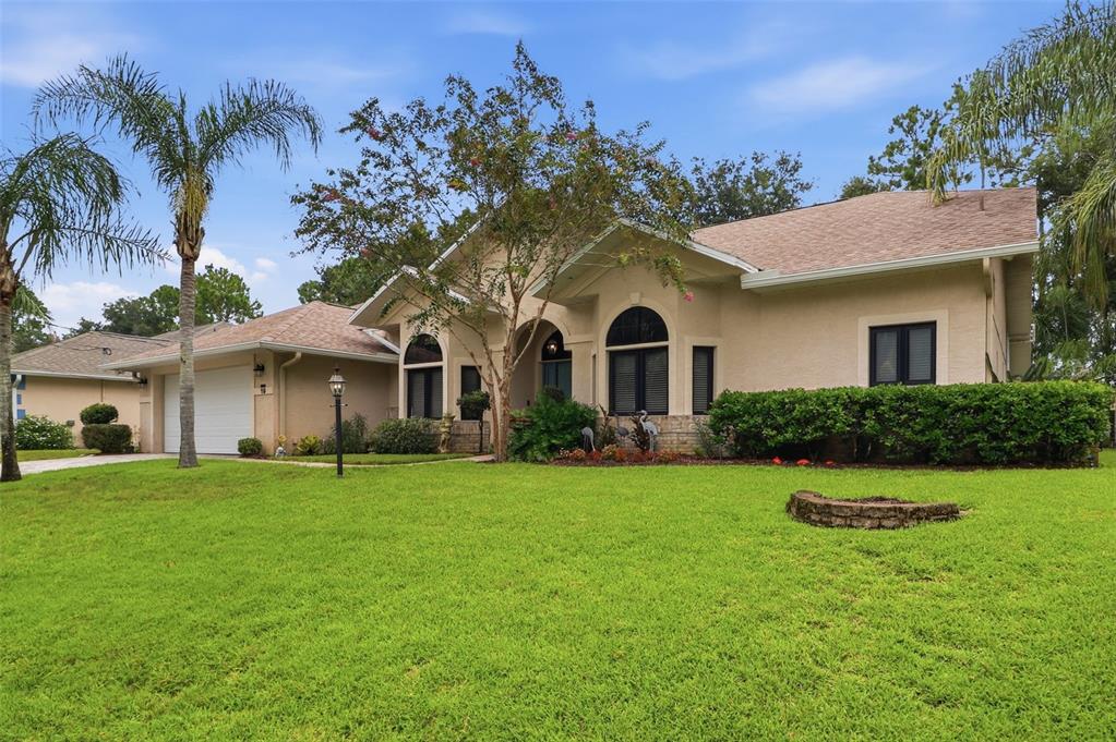 A single-story beige stucco house with a two-car garage, arched windows, and a front lawn — 19 WOODGUILD PLACE, PALM COAST, FL
