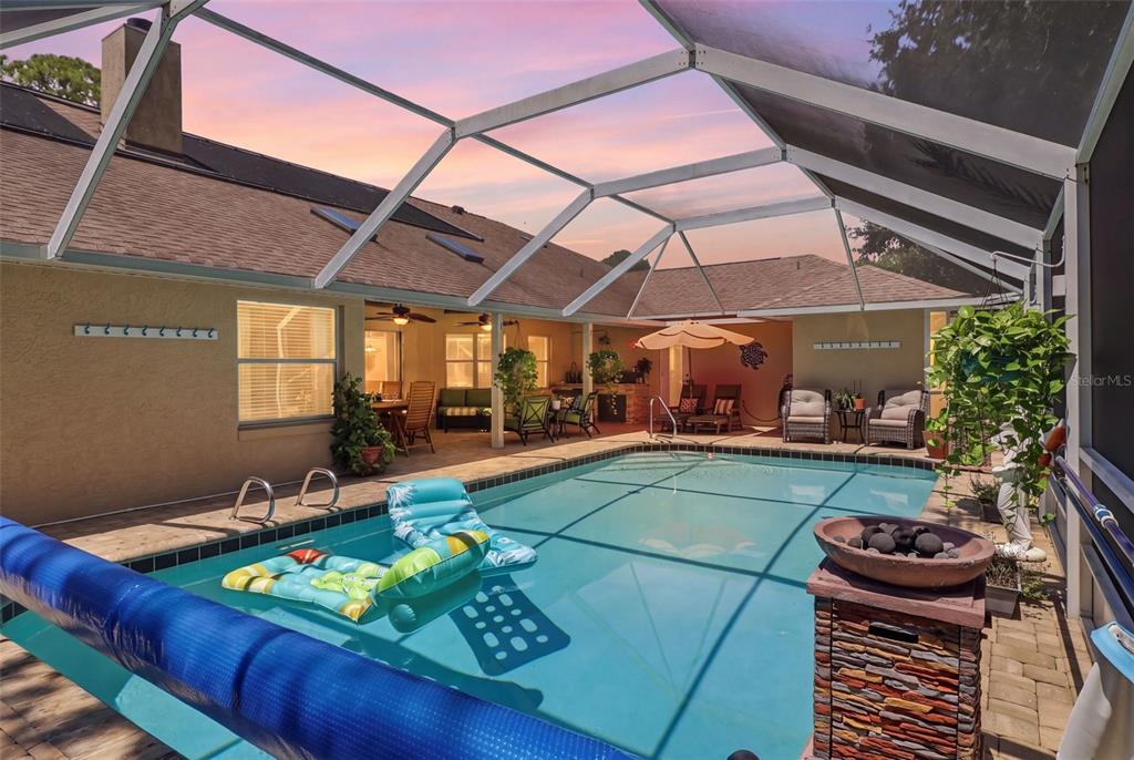 A screened-in patio features a swimming pool with floating rafts and outdoor seating areas — 19 WOODGUILD PLACE, PALM COAST, FL