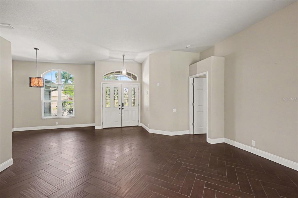 An empty room features dark herringbone wood flooring, white double entry doors, and arched windows — 11920 OAK RIDGE DRIVE, PARRISH, FL