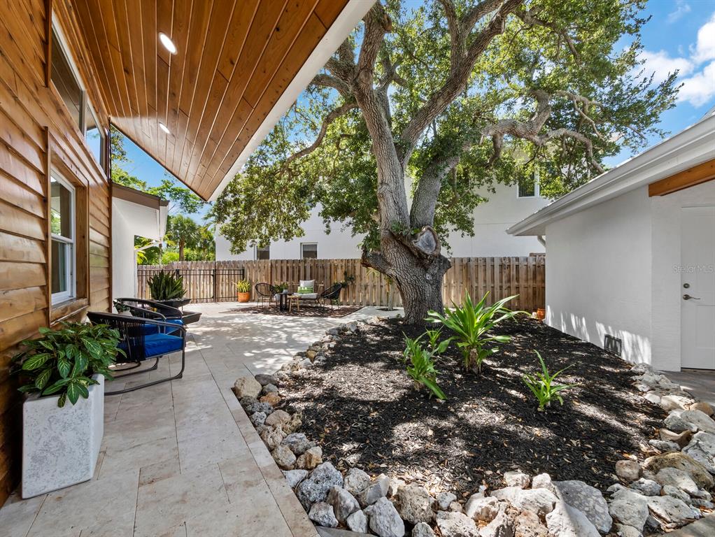 A patio with stone flooring, outdoor seating, and a large tree in a landscaped bed — 430 ISLAND CIRCLE, SARASOTA, FL
