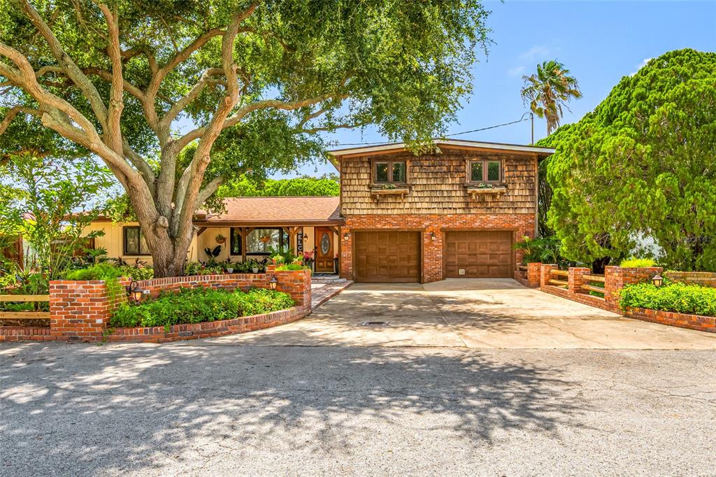 A two-story house with a brick and wood-shingled exterior, two garages, and a large tree — 1488 LACONIA DRIVE E, CLEARWATER, FL