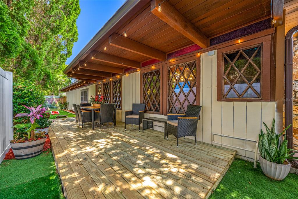 A wooden deck with outdoor furniture sits under a covered patio attached to a house — 1488 LACONIA DRIVE E, CLEARWATER, FL