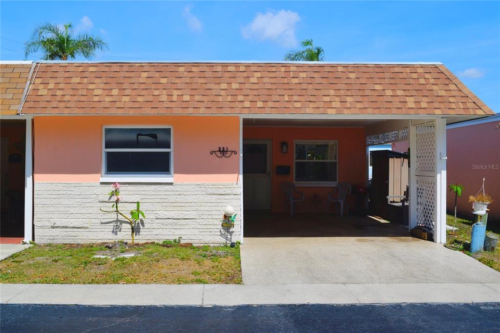 A single-story peach-colored house features a brown shingled roof, a carport, and stone siding — 331 SKY LOCH DRIVE W, DUNEDIN, FL