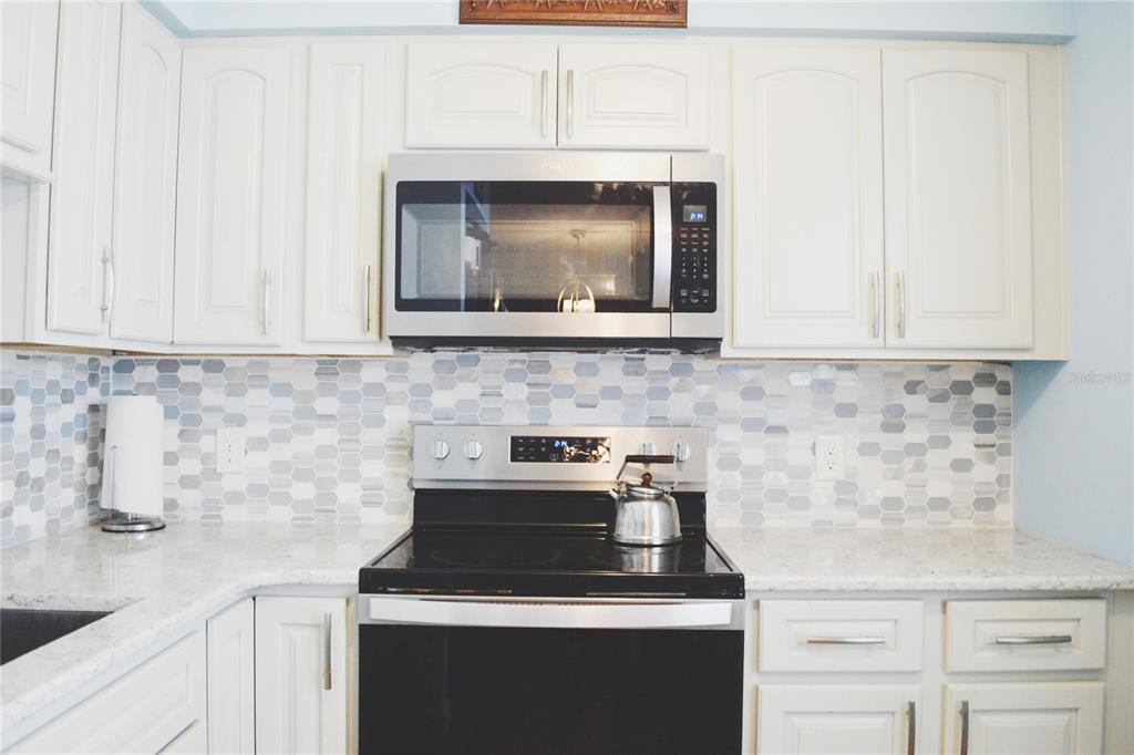 A kitchen with white cabinets, stainless steel appliances, and a mosaic tile backsplash — 331 SKY LOCH DRIVE W, DUNEDIN, FL