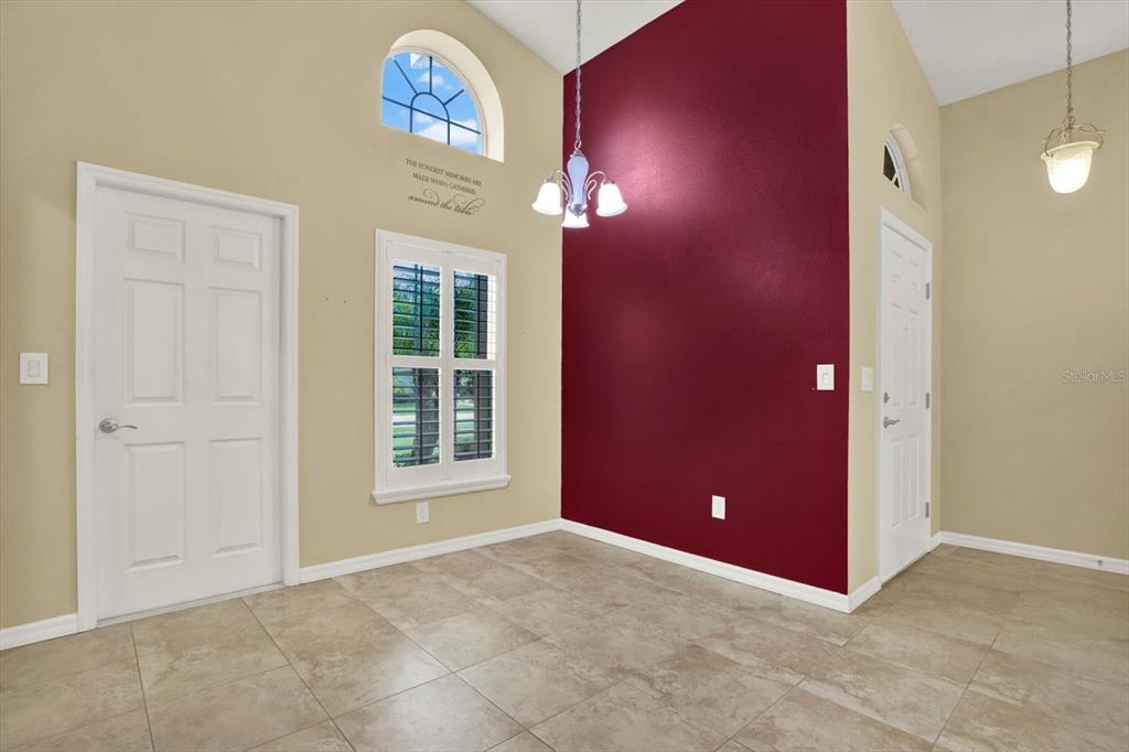 A dining area features tile floors, a vaulted ceiling, a red accent wall, and two chandeliers — 12922 PAYNE STEWART WAY, HUDSON, FL