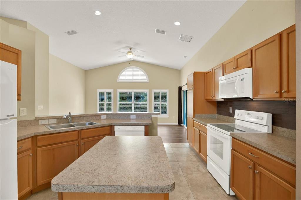 A kitchen with wood cabinets, laminate countertops, a center island, and white appliances — 12922 PAYNE STEWART WAY, HUDSON, FL