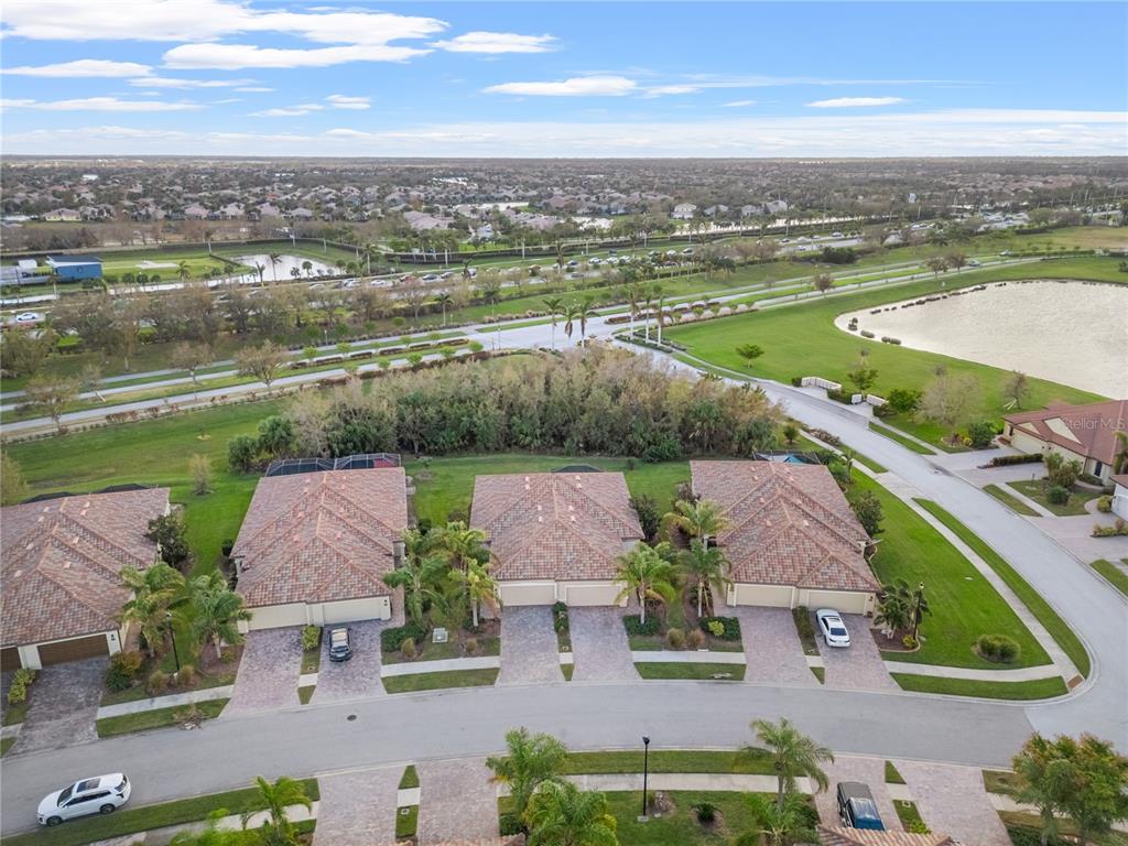 An aerial view shows three suburban houses with tiled roofs and driveways near a lake — 19874 BENISSIMO DRIVE, VENICE, FL