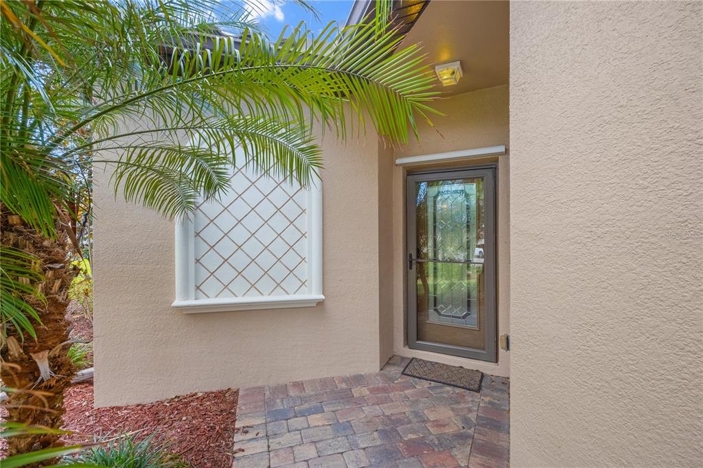 A beige stucco home entrance features a glass storm door and a decorative lattice window — 19874 BENISSIMO DRIVE, VENICE, FL