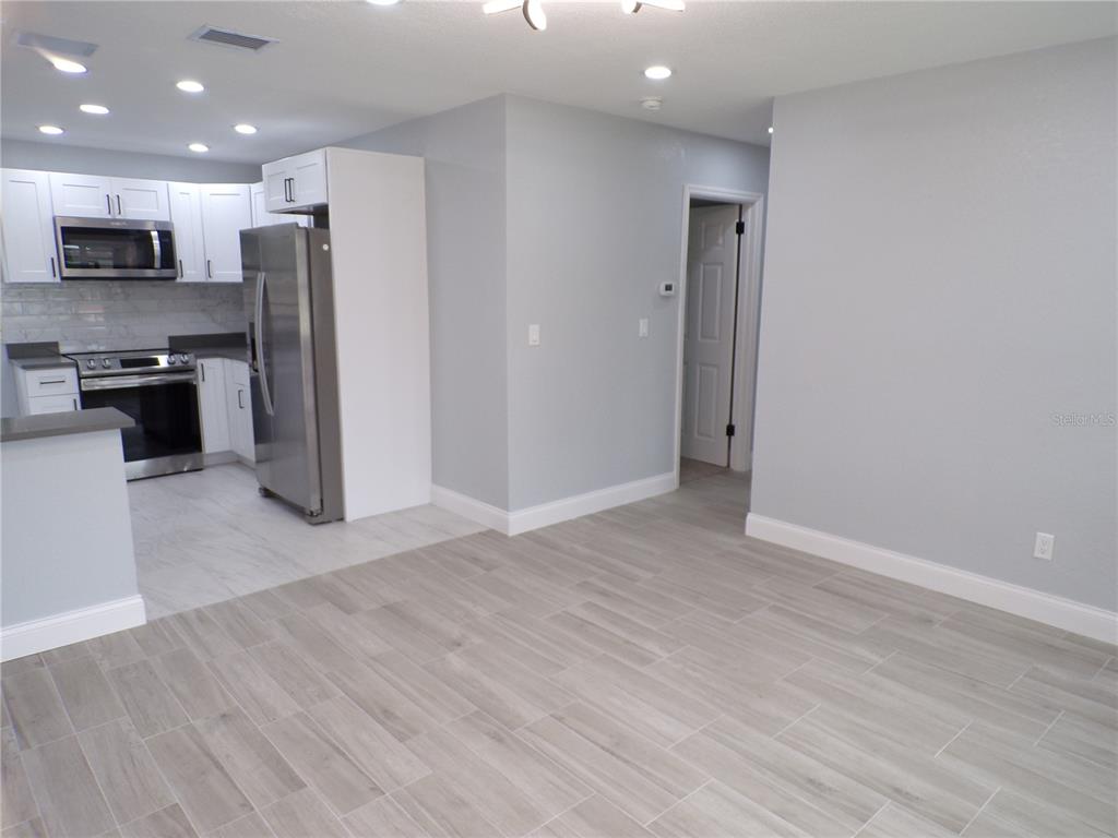 A kitchen with stainless steel appliances and white cabinets opens into a light-floored living area — 13674 120TH LANE, SEMINOLE, FL