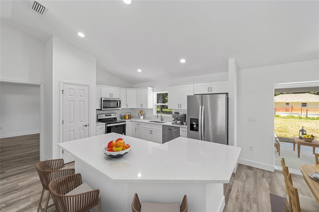 A bright kitchen features white cabinets, stainless steel appliances, and a large quartz-topped island — 5861 NW 64TH STREET, OCALA, FL