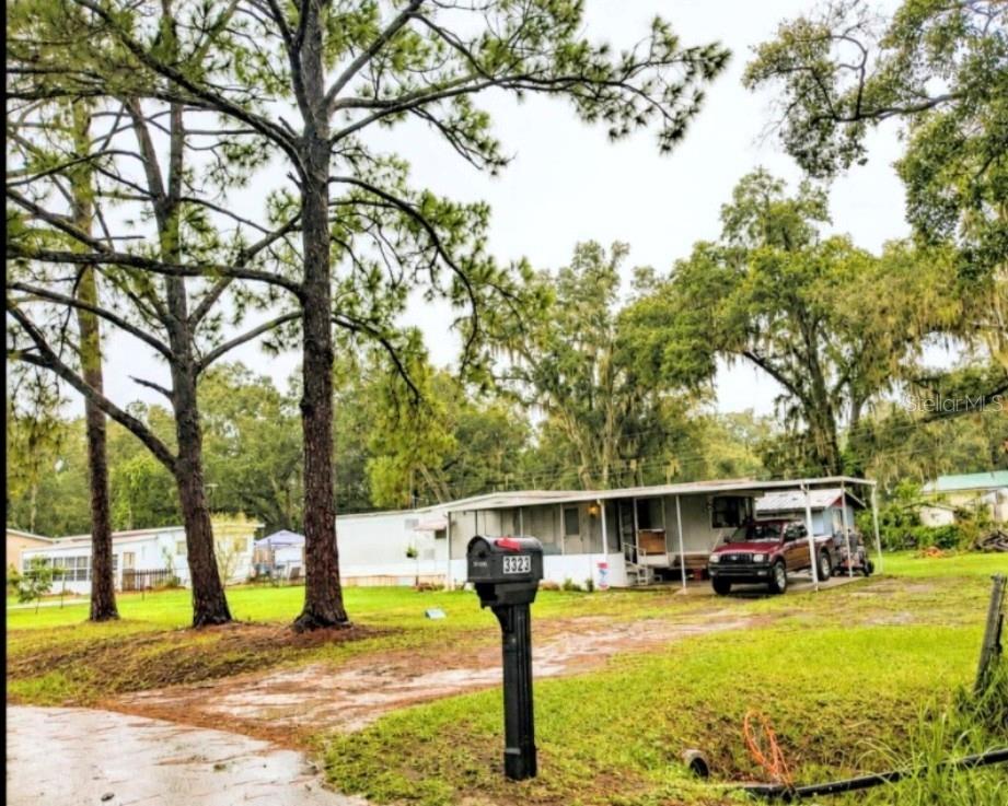 A single-story mobile home with a metal carport sits on a grassy lot with trees — 3323 J AND J MANOR ROAD, LAKELAND, FL