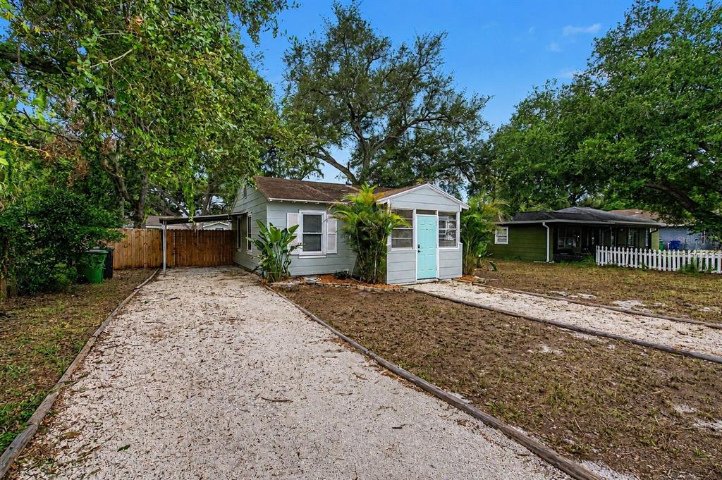 A light blue cottage with a gravel driveway and a screened front porch under trees — 3208 W HARTNETT AVENUE, TAMPA, FL