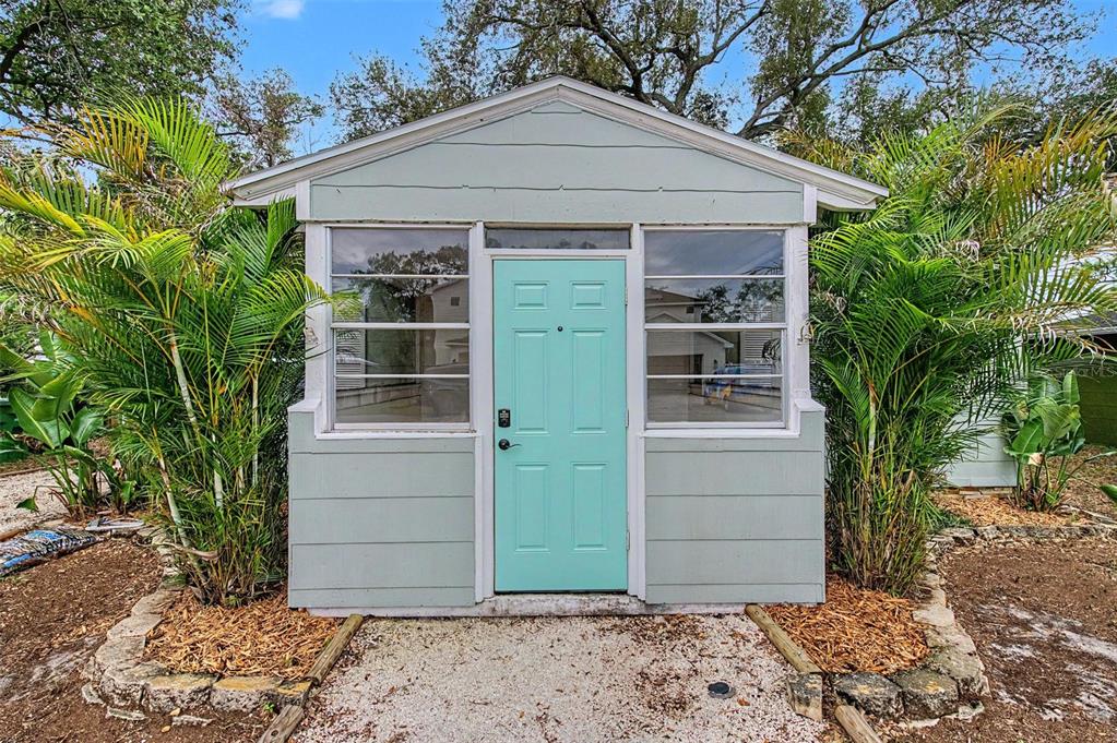 A light green shed with a matching door and large windows sits in a landscaped yard — 3208 W HARTNETT AVENUE, TAMPA, FL