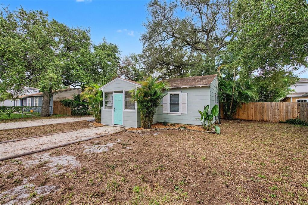 A small, light-green cottage with a turquoise front door sits on a grassy lot — 3208 W HARTNETT AVENUE, TAMPA, FL