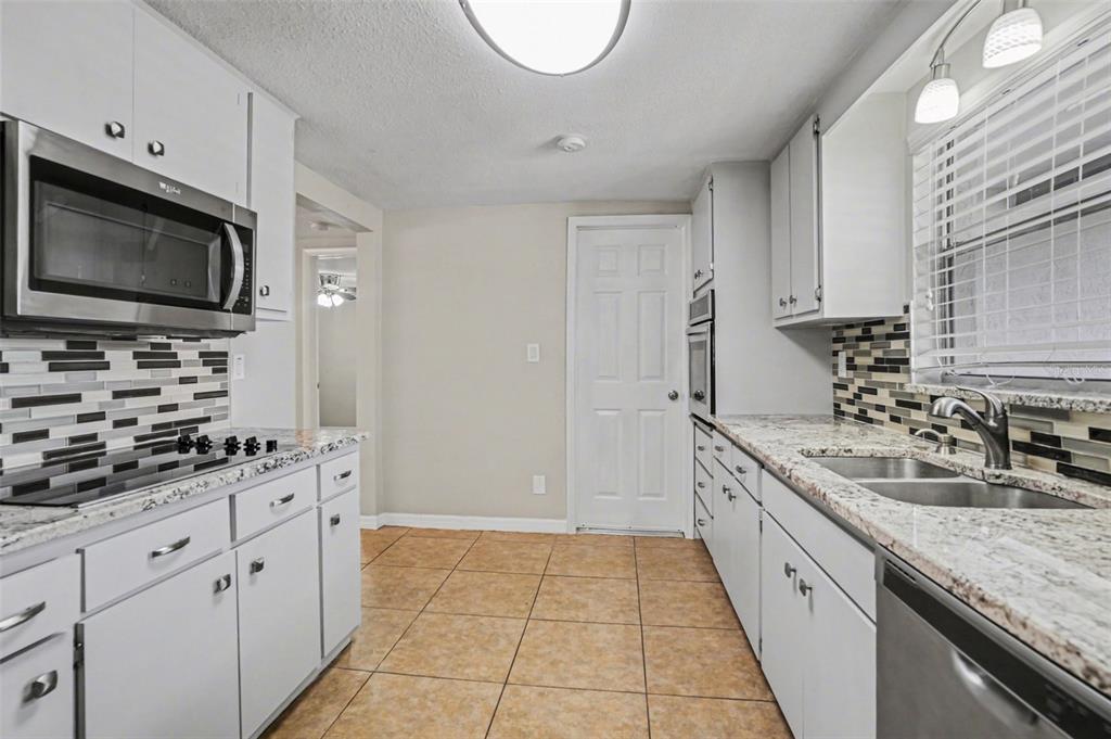A kitchen features white cabinets, granite countertops, a tiled backsplash, and stainless steel appliances — 8006 MIMOSA DRIVE, PORT RICHEY, FL