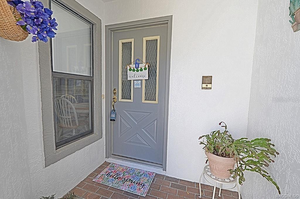 A gray front door with a decorative sign sits beside a window and a potted plant — 3371 S BELGRAVE DRIVE, INVERNESS, FL