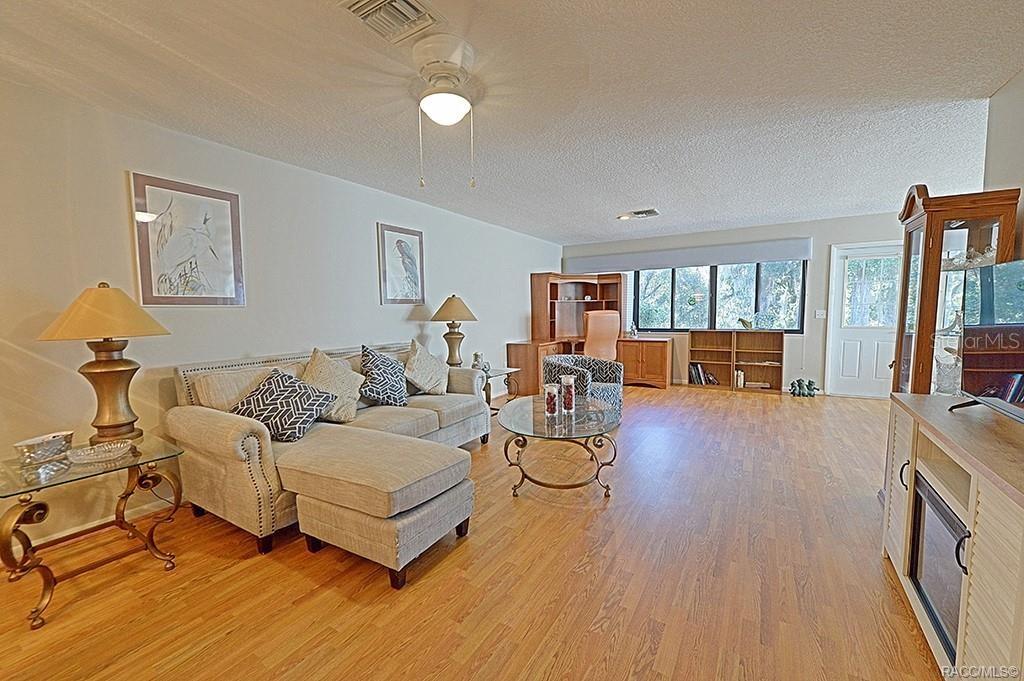 A living room features light wood flooring, a beige sectional sofa, and a glass coffee table — 3371 S BELGRAVE DRIVE, INVERNESS, FL