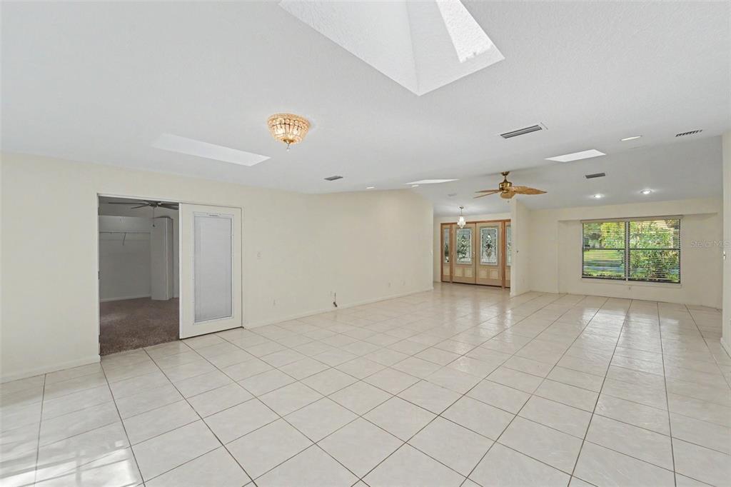 A bright, open-concept living area features white tile floors, a ceiling fan, and multiple skylights — 2057 BRENT PLACE, PALM HARBOR, FL