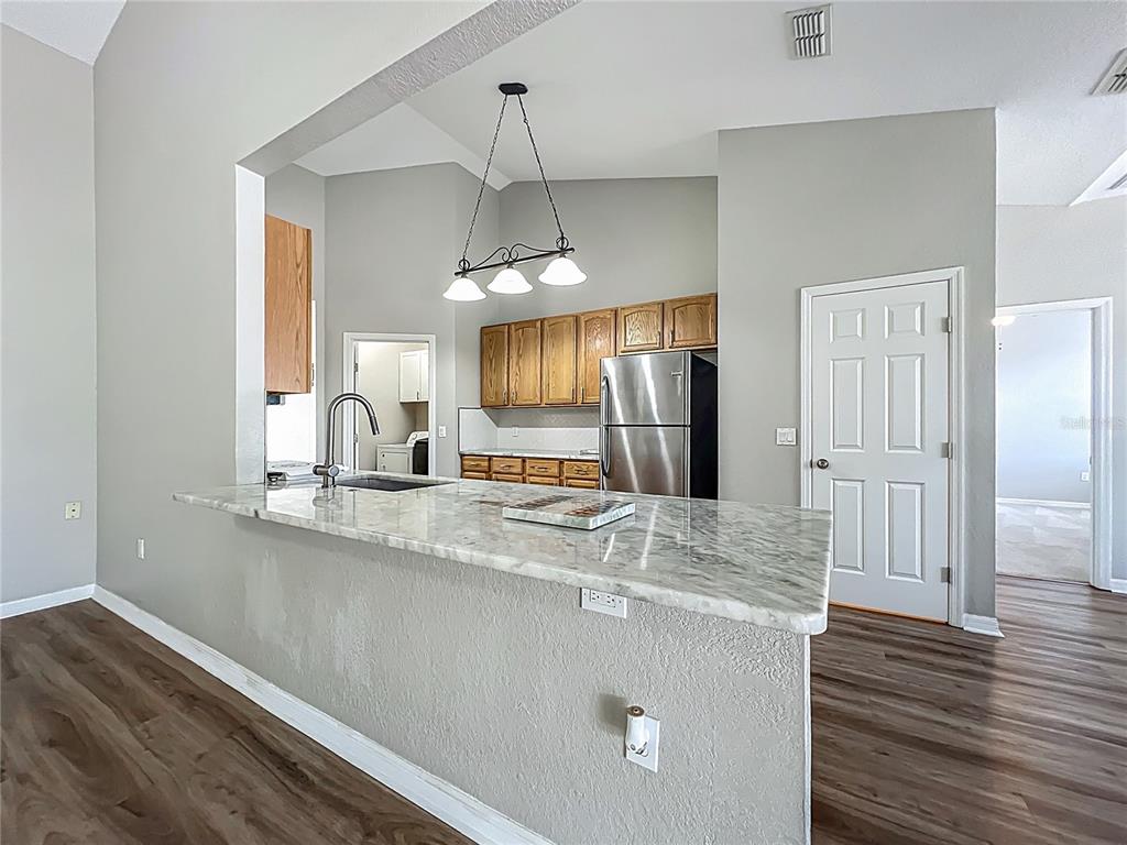 An open-concept living area features vaulted ceilings, wood-look flooring, and a kitchen pass-through window — 301 TERRANOVA BOULEVARD, WINTER HAVEN, FL