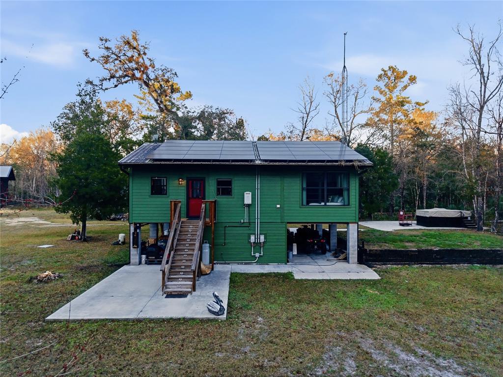 An elevated green house with a screened porch and wooden stairs sits on a grassy lot — Track 79 CLAYTON ROAD, CEDAR KEY, FL